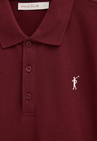 Bordeauxrood polohemd met drie knopen, een puntige kraag, wit geborduurd polo spelerlogo en een "Polo Club" label in maat small.