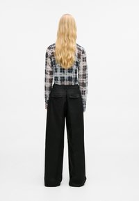 Transparente Bluse mit langen Ärmeln im schwarz-weißen Karomuster, kombiniert mit hochtaillierten, schwarzen weit geschnittenen Hosen mit Rückentaschen.