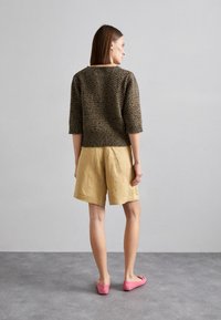 Maglione marrone lavorato a maglia, pantaloni corti di lino beige e scarpe slip-on rosa, visti da dietro. Il maglione ha una vestibilità ampia e un motivo testurizzato.
