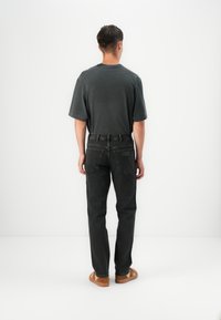 Mustad denim püksid sirge lõikega, millele on pandud selga lõdva tumesinise T-särk, vaadatud selja tagant. Ahned pruunad jalatsid.