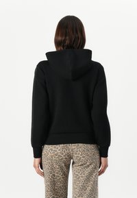 Zwarte hoodie met een kangaroo zak, ribbels bij de mouwen en een capuchon. Draagt met beige broeken met een panterprint. Soepele textuur, casual ontwerp.