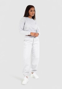 Hellgrauer Baumwoll-Sweatshirt und passende Sweatpants mit gerippten Bündchen. Das Model trägt weiße Sneaker; minimalistische Markenkennzeichnung auf dem Sweatshirt.