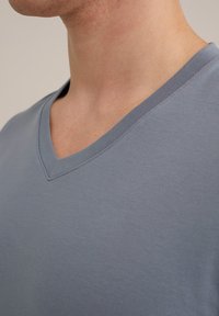 Siva majica s kratkimi rokavi in V-izrezom. Izdelana iz gladkega bombaža, z blagim odnosom in klasičnim krojem.