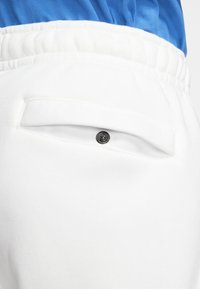 Vita sweatpants med en bakficka med horisontell öppning och en synlig svart tryckknapp. Strukturerad tyg med elastisk midja.