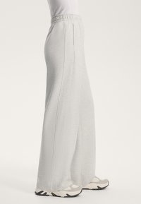 Svetlo sivi, visoki široki hlače iz mehkega materiala, z stranskimi žepi in teksturirano površino. V kombinaciji z svetlimi supergami.