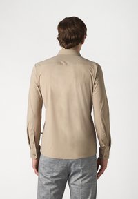 Beige långärmad skjorta med rak krage, knappmanschetter och en mjuk textur. Matchad med grå mönstrade byxor.