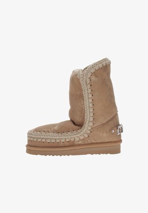 Stivale alla caviglia in pelle scamosciata color cognac con rifinitura intrecciata, finitura metallica, punta arrotondata e piccolo dettaglio decorativo in metallo sul lato.