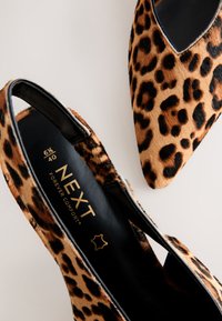 Paire de ballerines pointues à imprimé léopard avec intérieur noir et marquage doré "NEXT Forever Comfort" sur la semelle intérieure d'une chaussure.