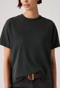 Μαύρο βαμβακερό t-shirt με κοντά μανίκια, στρογγυλή λαιμόκοψη και άνετη εφαρμογή. Φορεμένο με καφέ ζώνη, που διαθέτει λεπτομέρεια χρυσής αγκράφας.