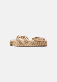 Tan platform sandals with woven rope detailing, featuring dual straps and a textured sole. Thick, braided outsole provides added height.