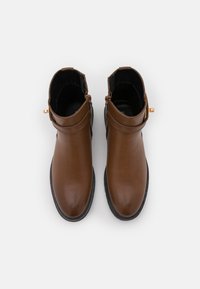 Bottes de cheville en cuir marron avec une texture lisse, un bout rond, un détail de boucle sur le côté et une semelle en caoutchouc noire.