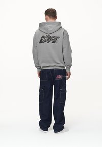 Szara bluza z kapturem z nadrukiem "NEVER TOO LATE" na plecach. Do tego ciemne dżinsowe spodnie cargo z bocznymi kieszeniami i detalem z logo.