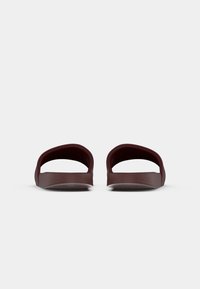 Sandales à enfilage ouvertes de couleur bordeaux avec une finition lisse et mate et un design de sangle incurvée. Semelle intérieure texturée et semelle rembourrée pour le confort.