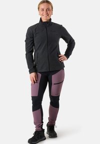 Mörkgrå zip-up jacka med hög krage, som är kombinerad med svarta och mauve stretchbyxor med dragkedjefickor och knälappar.