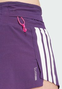 Ljubičaste kratke hlače od teksturiranog materijala, s bijelim dizajnom tri pruge, bočnim prorezom i ružičastom petljom za zatvaranje. Uključuje logo "ClimaCool".