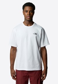 Hvid bomulds T-shirt med et diskret sort logo på venstre bryst, rund halsudskæring og korte ærmer, parret med røde cargo shorts.