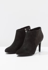 Botines negros que presentan una combinación de ante y paneles de malla texturizada, puntera afilada y un tacón alto y delgado. Detalle de cremallera en el lateral.