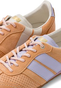 Baskets basses en daim couleur camel avec des bandes en cuir violet pastel, des lacets rose pâle et un logo doré sur la languette.