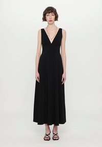 Zwarte, mouwloze maxi-jurk met een V-hals en A-lijn silhouet. Gladde stof, vloerlengte, gecombineerd met zwarte sandalen met bandjes.