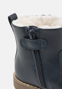 Bota de tobillo de cuero azul oscuro con cierre de cremallera, forro suave color crema, exterior texturizado y detalles de costura en contraste.