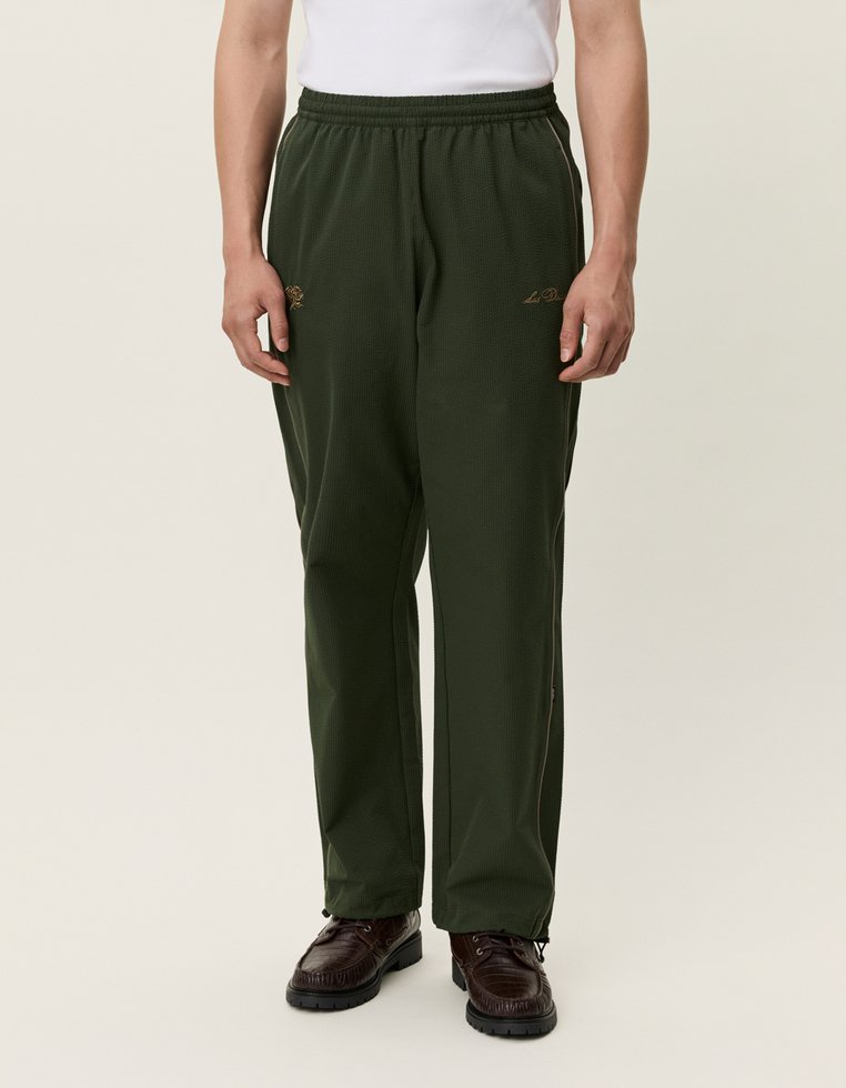 Tmavozelené, štruktúrované polyesterové nohavice s elastickým pásom. Obsahujú biele bočné pruhy a zlaté logo na nohavici.