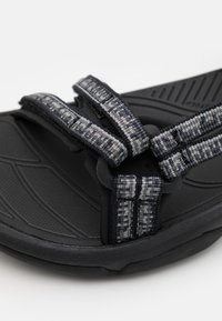 Black sandal featuring textured rubber sole, woven straps in gray and blue patterns, and adjustable closures for a secure fit.