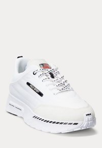 Bílé tenisky Polo Sport s černými akcenty loga, brandingem Ralph Lauren, nášivkou americké vlajky na jazyku a vzorovanou podrážkou.