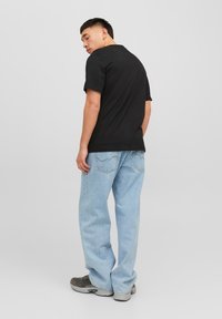 Black cotton t-shirt with short sleeves, paired with light blue denim jeans and gray sneakers, viewed from the back.