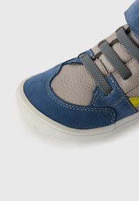 Baskets en daim bleu et en cuir gris avec des lacets gris et une semelle blanche. Présente des coutures et un accent jaune sur le côté. Design à bout arrondi.