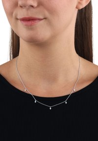 Collana d'argento con più fili delicati, accentuata da piccole gemme trasparenti. Indossata sopra un top nero a coste.