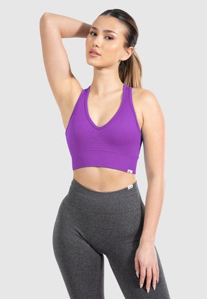 Purple ribbed sports bra with a V-neck design, featuring wide straps and a cropped length, paired with high-waisted gray leggings.