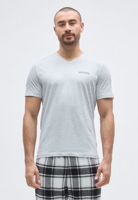 Grå v-hals t-shirt lavet af glat stof, med korte ærmer og en lille sort "GUESS"-logo på venstre side af brystet.