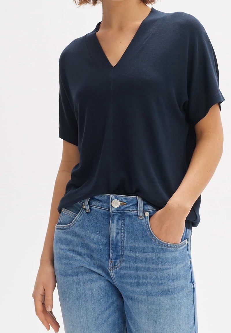Haut bleu marine à manches courtes avec un col en V, fabriqué en tissu lisse. Associé à un jean en denim bleu clair avec une coupe classique et des poches.