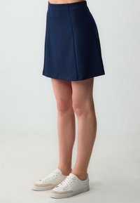 Gonna a pieghe blu navy con un design semplice a trapezio. Presenta una texture di tessuto morbido e una vita elastica per il massimo comfort. Abbinata a sneakers bianche.