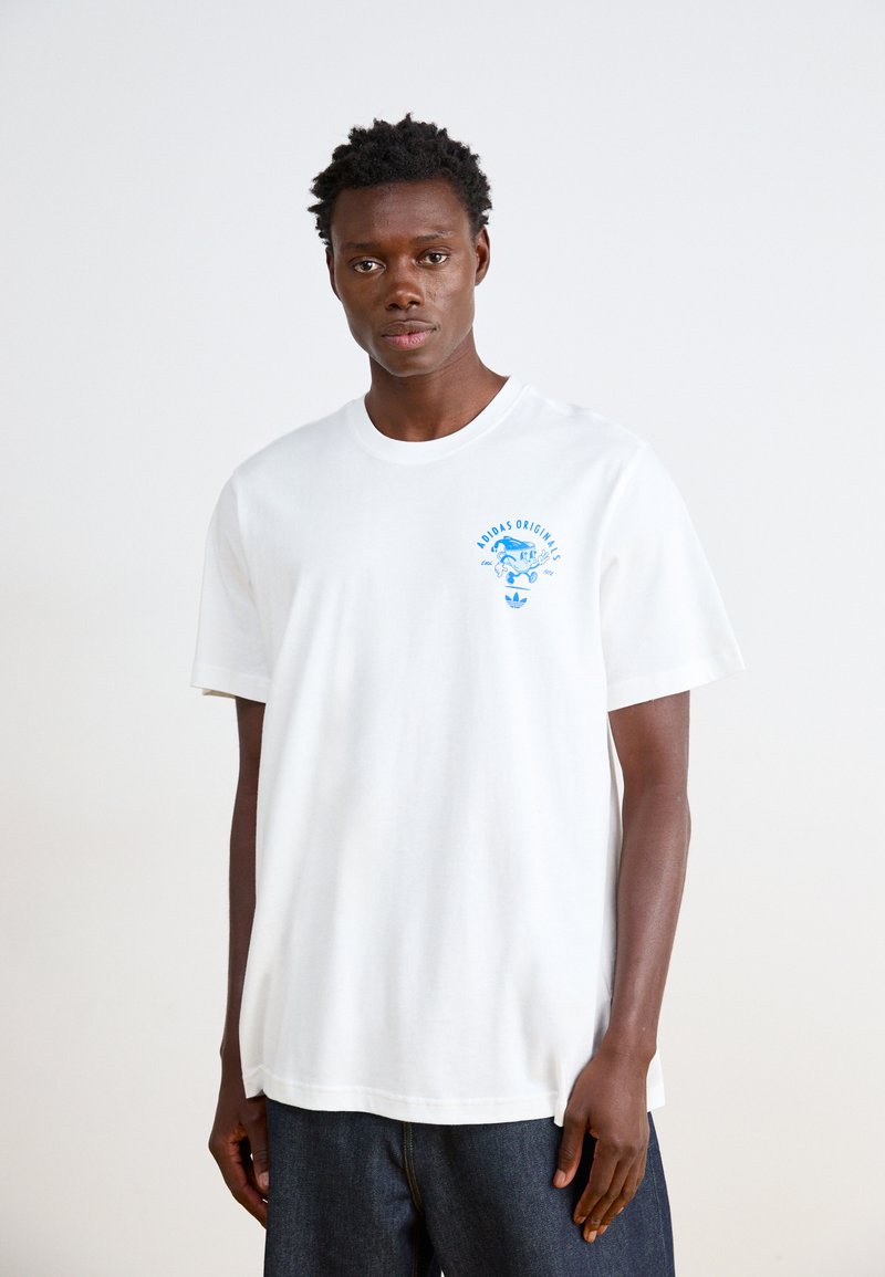 Λευκό βαμβακερό t-shirt με στρογγυλή λαιμόκοψη, κοντά μανίκια και μπλε γραφικό "Adidas Originals" στην αριστερή πλευρά του στήθους. Χαλαρή εφαρμογή, ομαλή υφή.