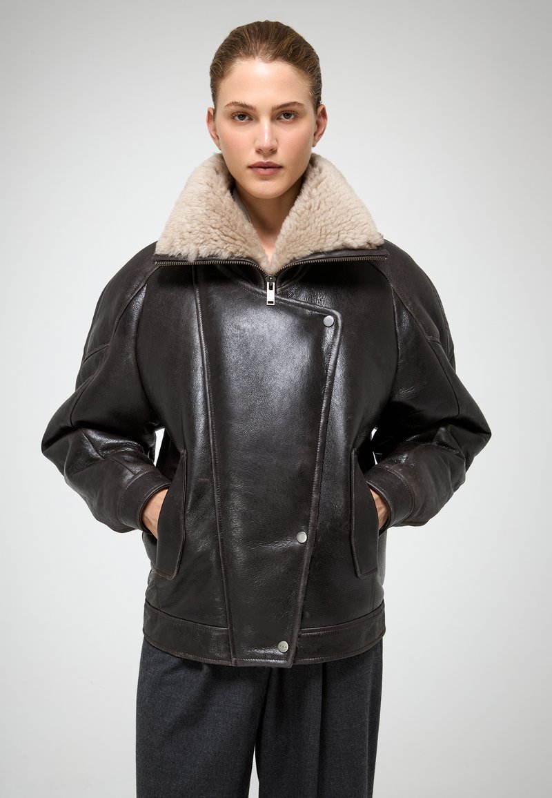 Bruine leren jacket met een grote beige bontkraag, ritsluiting, zijzakken en een matte textuur. Heeft een modern, oversized ontwerp.