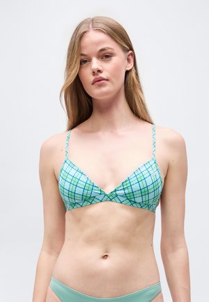 Mladá žena s dlhými blond vlasmi, ktorá má na sebe modro-zelený károvaný bikiny top a jednofarebné svetlozelené bikiny nohavičky.