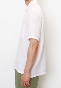 Witte linnen kraagloze shirt met korte mouwen, enkele borstzak en opgerolde mouwen, gemaakt van een lichtgewicht en iets gestructureerde stof.