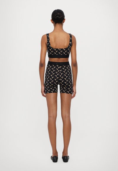 Svart treningssett bestående av en cropped topp og høyhårede shorts med et kremfarget halvmåne-mønster, glatt tekstur og elastisk midje.