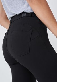 Mustat legginsit, joissa on korkea vyötärö ja takatasku. Kangas näyttää sileältä, siinä on hieman kiiltoa ja se on istuva malli.