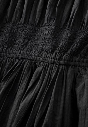 Robe noire à texture froncée, avec un smockage horizontal sur le buste et des plis fluides à l'ourlet. Tissu léger.