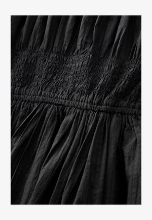 Black dress with gathered texture, featuring horizontal smocking along the bodice and flowing pleats at the hem. Lightweight fabric.