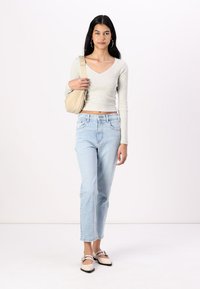 Nous avons un haut ajusté gris clair à manches longues, un jean droit taille haute bleu clair, un sac bandoulière beige et des ballerines bicolores avec des lanières.