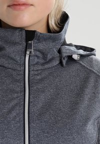 Šedá bunda na zip s vysokým límcem, vyrobená z texturované tkaniny. Má nastavitelnou kapuci a stříbrný kovový zip.
