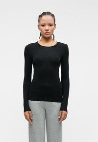 Czarny długi rękaw, dopasowany krój, okrągły dekolt, gładka faktura, noszony z szarymi spodniami w szerokim kroju. Prosty design, bez wzorów i widocznych akcentów.