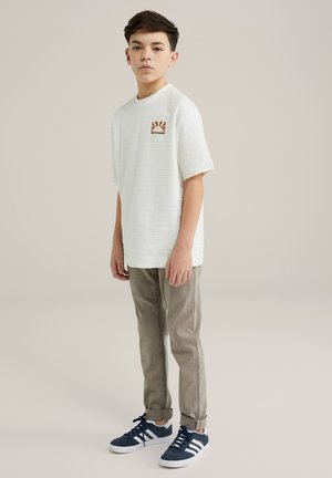 Lichtgroen gestreept T-shirt met een bruine zonlogo, gecombineerd met grijze broeken en blauwe sneakers met witte strepen. Casual pasvorm en ontwerp.