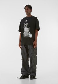 Sort oversized t-shirt med grafisk print af en kvinde, der holder blomster, parret med løse grå cargo-bukser og sorte sneakers.