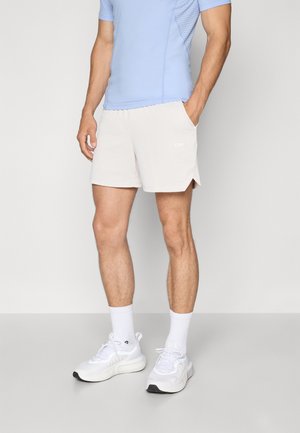 Shorts atletici de culoare bej deschis, cu deschideri laterale, asortați cu o cămașă ajustată de culoare albastru deschis, cu accente din plasă. Purtați cu pantofi atletici și șosete albe.