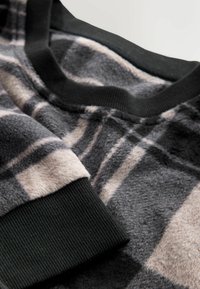 Nahaufnahme eines weichen Fleece-Stoffs mit grauem und beigem Karomuster sowie schwarzen Rippbündchen und -kragen.