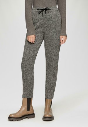Pantalon à chevrons gris avec une taille élastique et un cordon noir ; coupe ajustée, associé à des bottines marron à semelle épaisse.